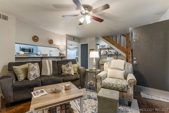 living room featuring ceiling fan, a textured ceiling, and dark wood-type flooring