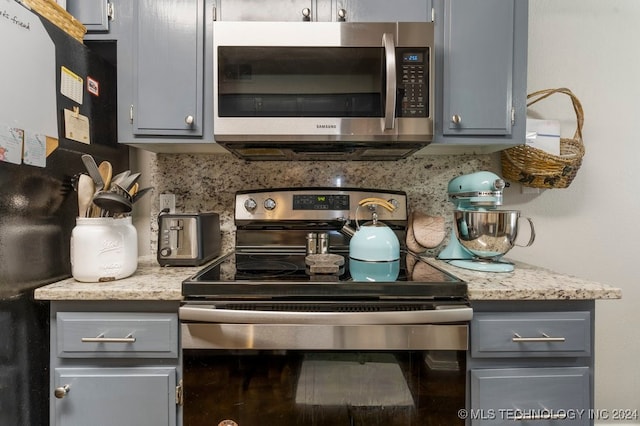 kitchen with tasteful backsplash, light stone countertops, appliances with stainless steel finishes, and gray cabinetry