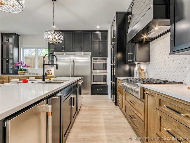 kitchen with hanging light fixtures, light stone countertops, appliances with stainless steel finishes, a notable chandelier, and custom range hood