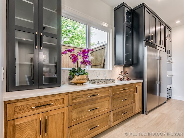 kitchen with light wood-type flooring, stainless steel built in refrigerator, double oven, and tasteful backsplash