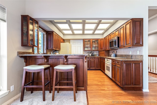 kitchen featuring white appliances, light hardwood / wood-style floors, kitchen peninsula, and backsplash