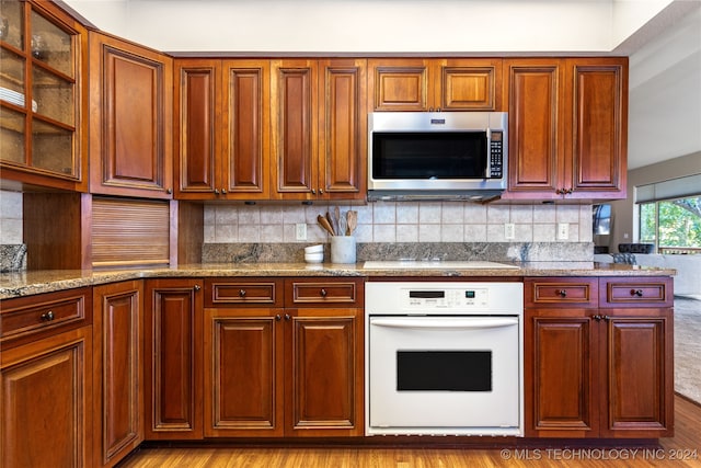 kitchen featuring light stone countertops, light wood-type flooring, white oven, decorative backsplash, and electric stovetop