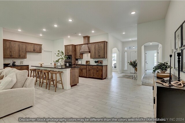 kitchen with stainless steel appliances, a kitchen island, light hardwood / wood-style flooring, custom exhaust hood, and a kitchen bar