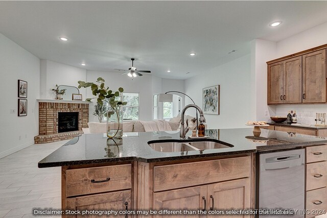 kitchen with dark stone countertops, a brick fireplace, sink, and stainless steel dishwasher