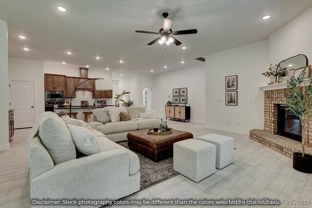 living room with a brick fireplace, sink, light hardwood / wood-style flooring, and ceiling fan