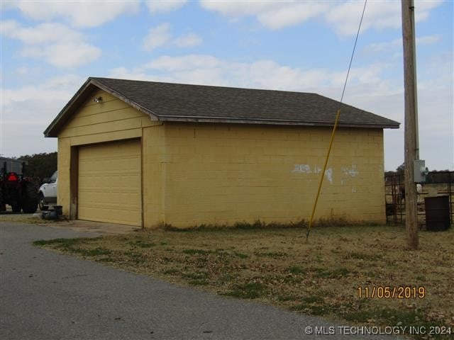 view of property exterior with dirt driveway, a shingled roof, concrete block siding, and an outdoor structure