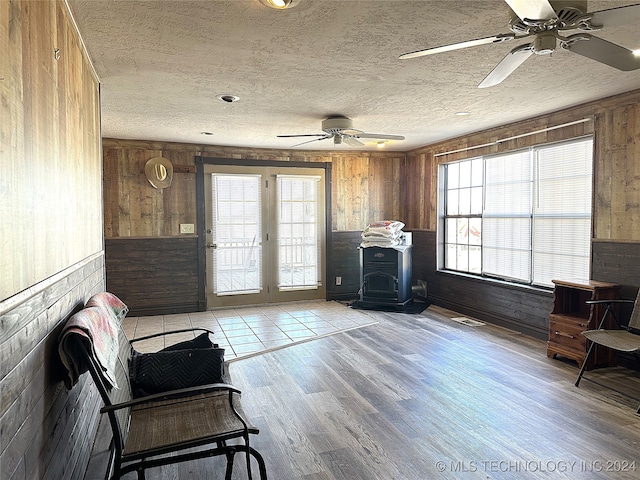 sitting room featuring ceiling fan, light wood-type flooring, wood walls, and a wood stove