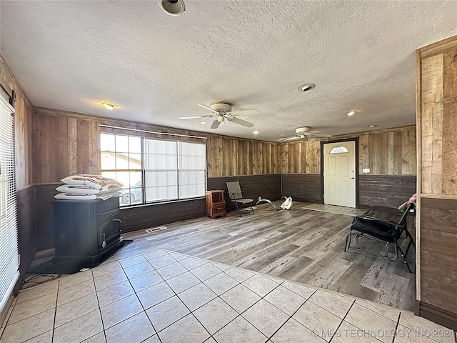 sitting room with wooden walls, a ceiling fan, light tile patterned floors, and a textured ceiling