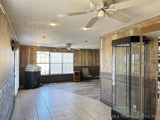 interior space with wood walls, a ceiling fan, a textured ceiling, and a wood stove
