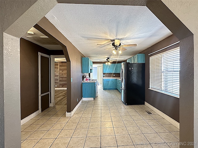 kitchen featuring ceiling fan, fridge, blue cabinetry, a textured ceiling, and light tile patterned floors