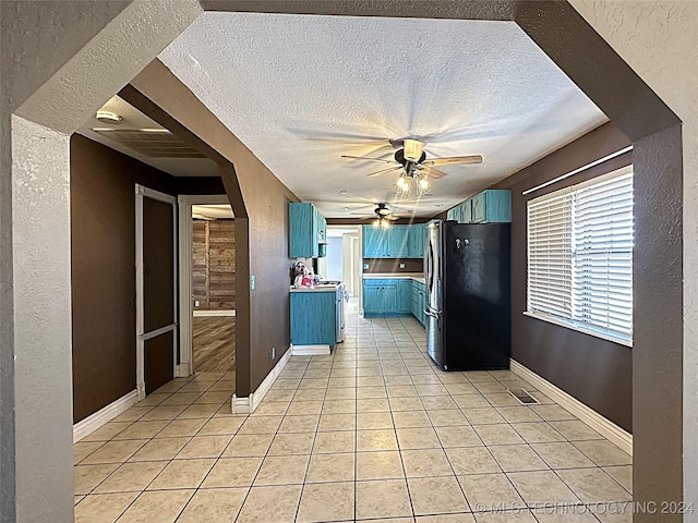 kitchen featuring light tile patterned flooring, a textured ceiling, freestanding refrigerator, and blue cabinetry