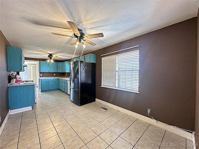 kitchen with light tile patterned floors, freestanding refrigerator, baseboards, blue cabinetry, and a ceiling fan