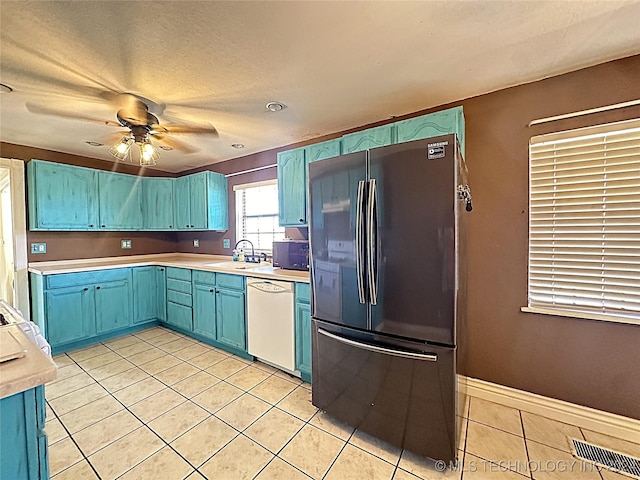kitchen featuring light tile patterned floors, white dishwasher, freestanding refrigerator, and blue cabinetry
