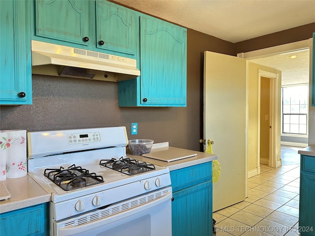 kitchen with white gas range, light tile patterned floors, blue cabinets, and under cabinet range hood