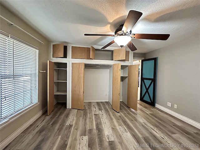 unfurnished bedroom featuring ceiling fan, wood-type flooring, multiple windows, a textured ceiling, and a closet