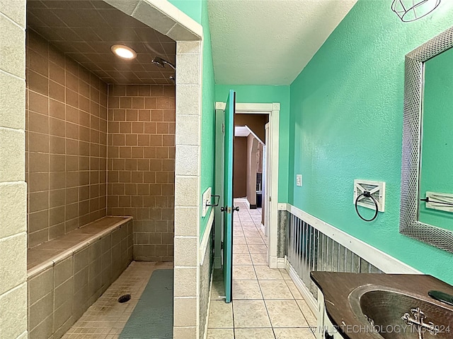 bathroom featuring a tile shower, tile patterned flooring, a textured wall, and vanity