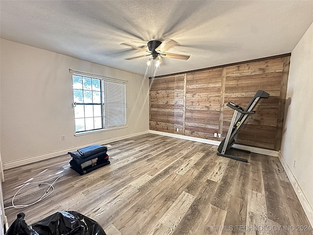 interior space with ceiling fan, a textured ceiling, hardwood / wood-style floors, and wooden walls