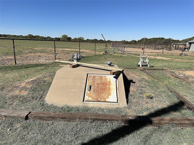 view of storm shelter with fence, a rural view, and a lawn