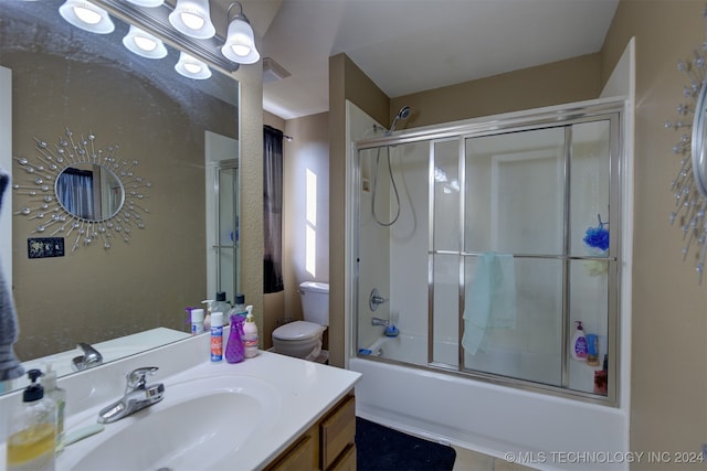 full bathroom with enclosed tub / shower combo, vanity, and toilet