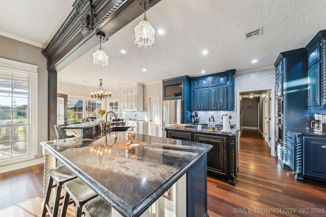 kitchen with blue cabinets, a notable chandelier, a sink, stainless steel appliances, and a large island with sink