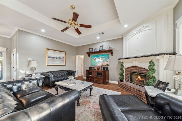 living area with wood finished floors, visible vents, a fireplace, crown molding, and a raised ceiling