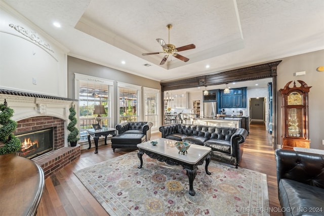 living room with a tray ceiling, a brick fireplace, wood finished floors, and crown molding