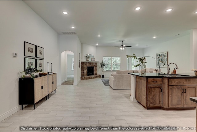 kitchen featuring a brick fireplace, light wood-type flooring, sink, and ceiling fan