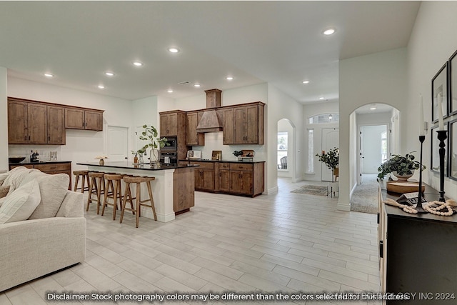 kitchen featuring custom exhaust hood, a kitchen island, stainless steel appliances, a breakfast bar area, and light hardwood / wood-style floors