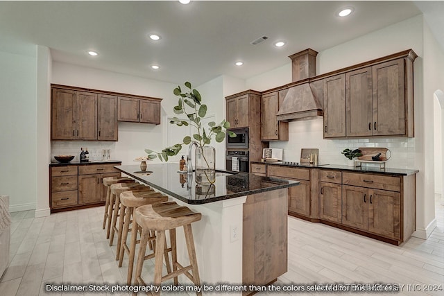 kitchen with an island with sink, sink, dark stone counters, appliances with stainless steel finishes, and backsplash