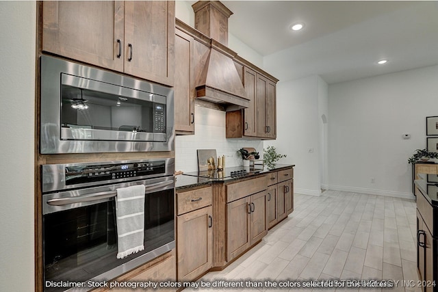 kitchen featuring dark stone countertops, premium range hood, stainless steel appliances, and backsplash