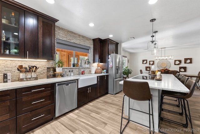 kitchen featuring light wood-type flooring, pendant lighting, appliances with stainless steel finishes, dark brown cabinets, and a kitchen breakfast bar