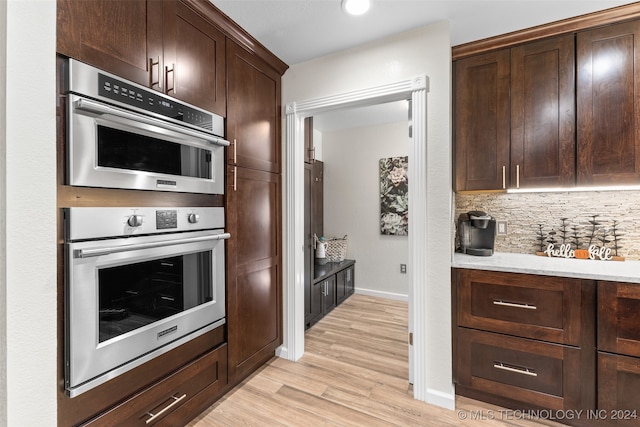 kitchen with stainless steel double oven, backsplash, dark brown cabinetry, and light hardwood / wood-style flooring