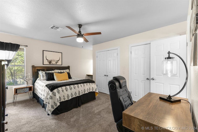 bedroom with ceiling fan, multiple closets, carpet, and a textured ceiling