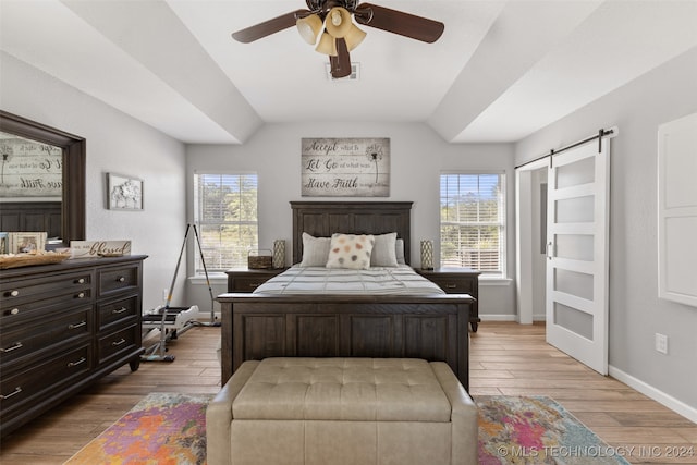 bedroom with light hardwood / wood-style flooring, a barn door, multiple windows, and lofted ceiling