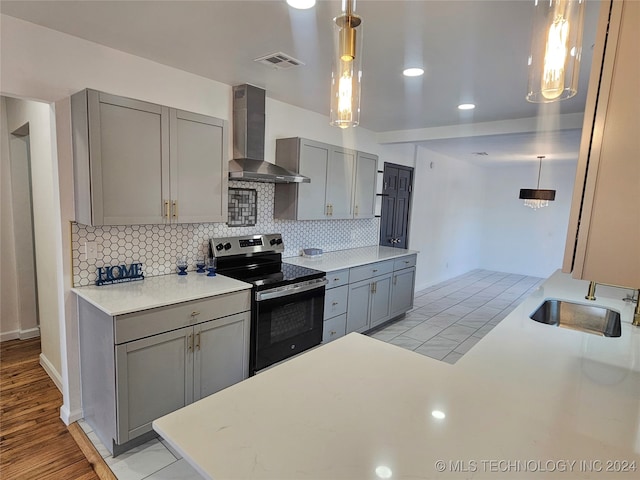 kitchen featuring wall chimney exhaust hood, gray cabinets, decorative light fixtures, and stainless steel electric range