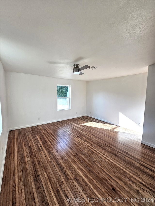 empty room with ceiling fan, dark wood-type flooring, and a textured ceiling