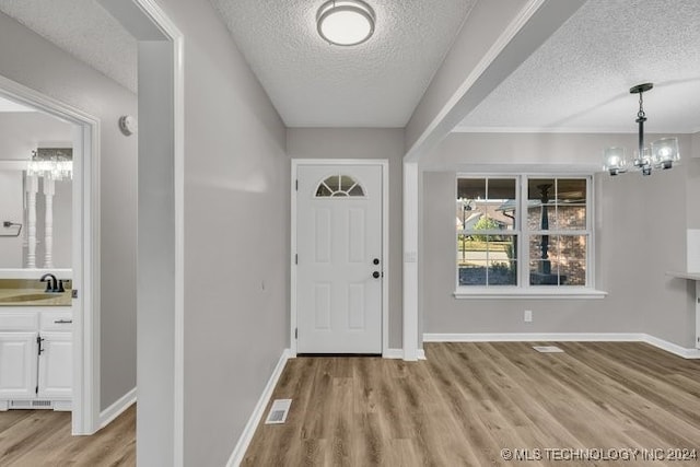 foyer entrance with light wood-type flooring, sink, an inviting chandelier, and a textured ceiling