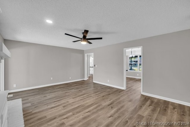 unfurnished living room featuring ceiling fan with notable chandelier, hardwood / wood-style floors, and a textured ceiling