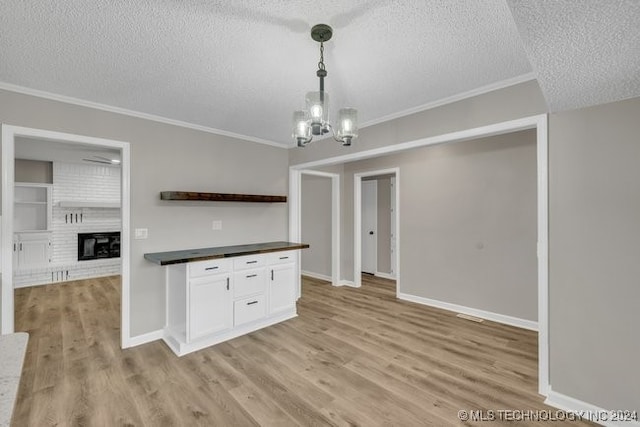 kitchen featuring white cabinetry, crown molding, light hardwood / wood-style flooring, decorative light fixtures, and a textured ceiling