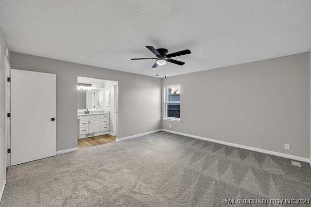 unfurnished bedroom featuring light carpet, ceiling fan, a textured ceiling, and ensuite bath