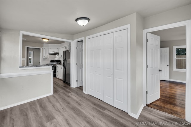 kitchen with stainless steel fridge, black stove, tasteful backsplash, light hardwood / wood-style flooring, and white cabinets