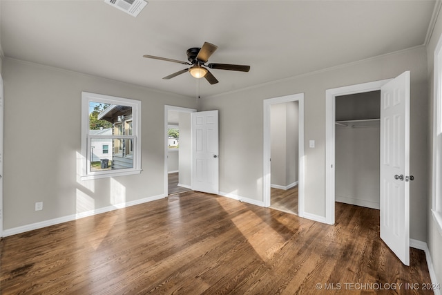 unfurnished bedroom featuring ceiling fan, a closet, dark hardwood / wood-style flooring, a walk in closet, and ornamental molding