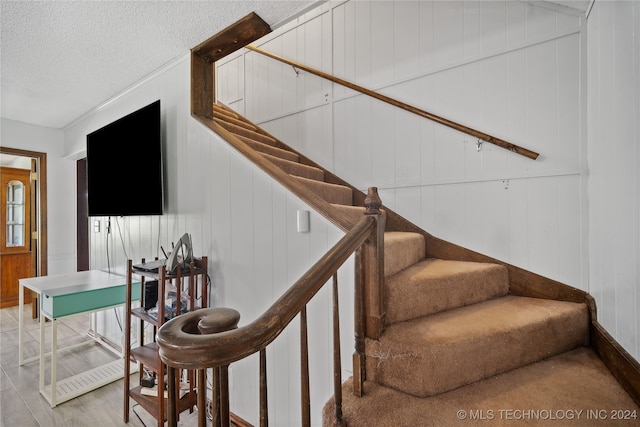 stairs featuring wood-type flooring, a textured ceiling, and wooden walls