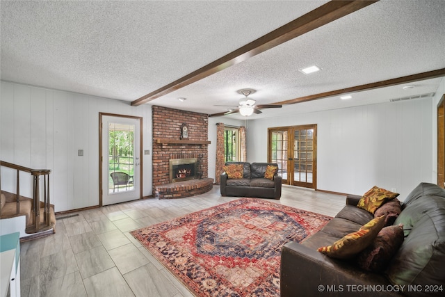 living room featuring beam ceiling, ceiling fan, a brick fireplace, a textured ceiling, and wooden walls