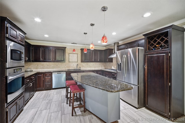 kitchen featuring appliances with stainless steel finishes, sink, wall chimney range hood, decorative light fixtures, and a center island