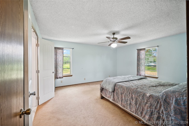 bedroom with multiple windows, ceiling fan, light colored carpet, and a textured ceiling