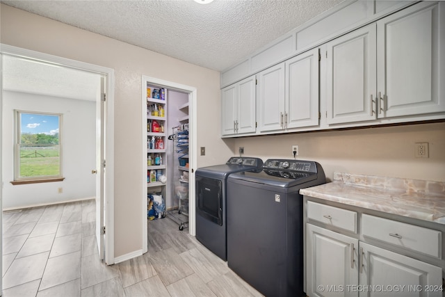 laundry area with cabinets, a textured ceiling, and washer and clothes dryer