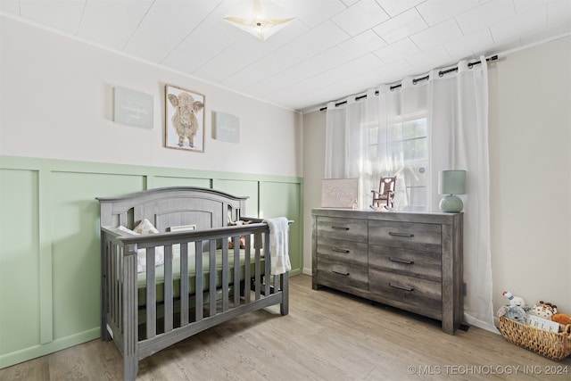 bedroom with crown molding, a crib, and light hardwood / wood-style flooring