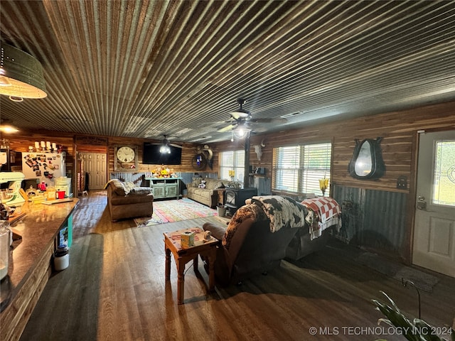 living room featuring ceiling fan, hardwood / wood-style floors, wooden walls, and a wood stove