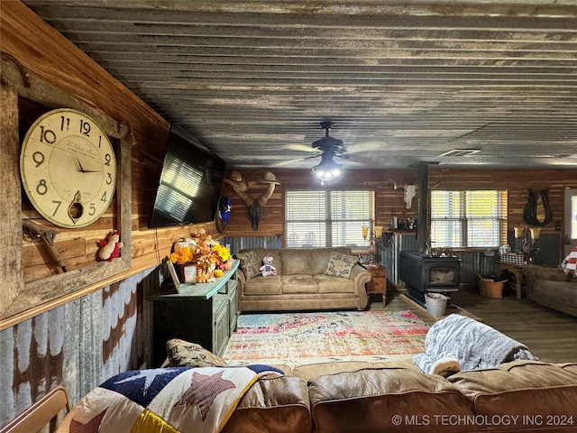 living room with wood walls, ceiling fan, hardwood / wood-style flooring, and a wood stove